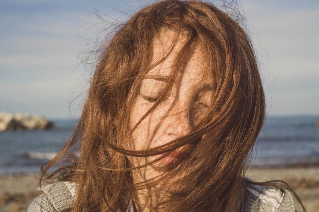 A dreamy woman with closed eyes and windy hair with a beach the background representing the magian brand archetype