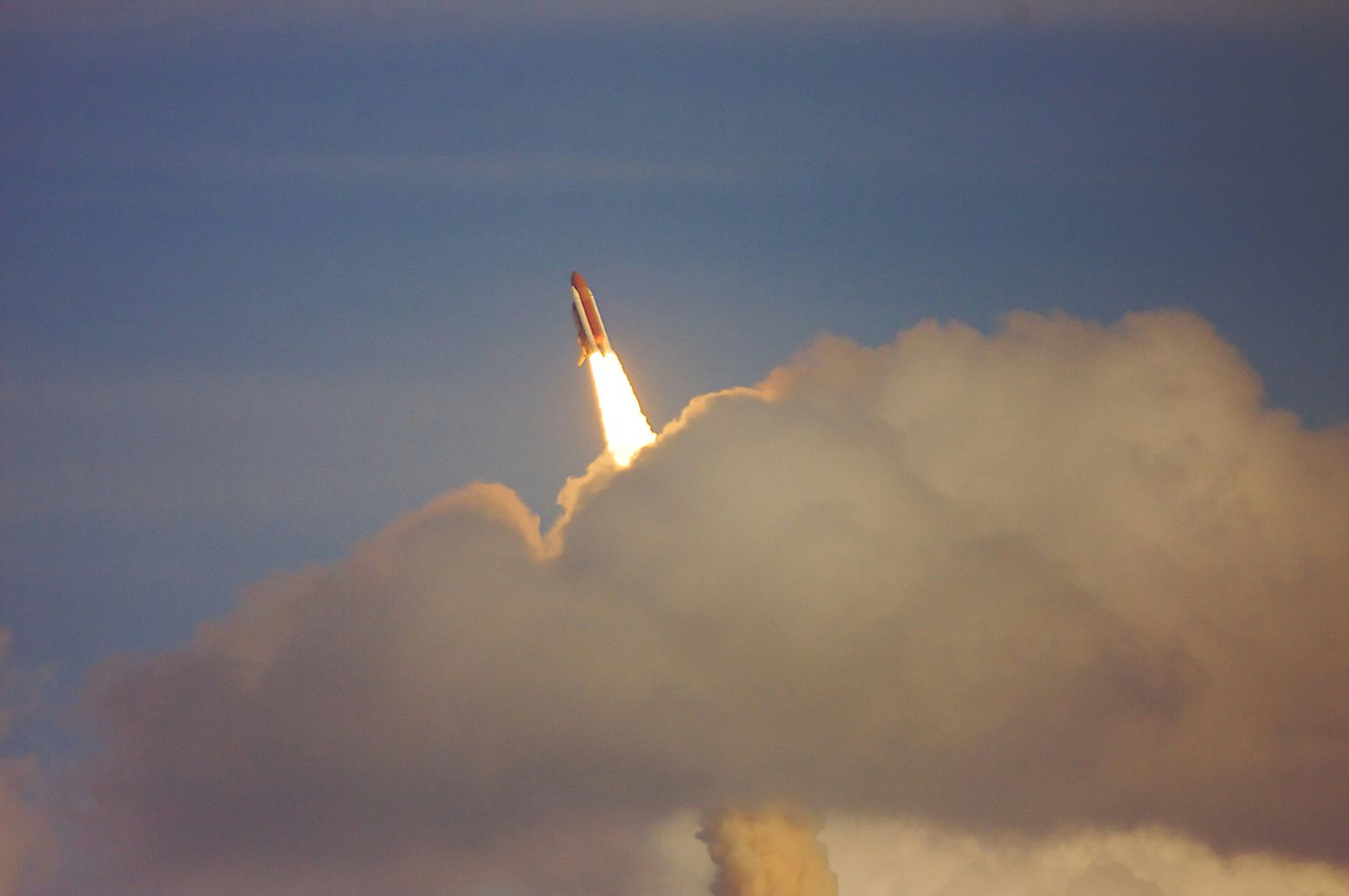 A picture of a rocket in the sky passing behind a cloud